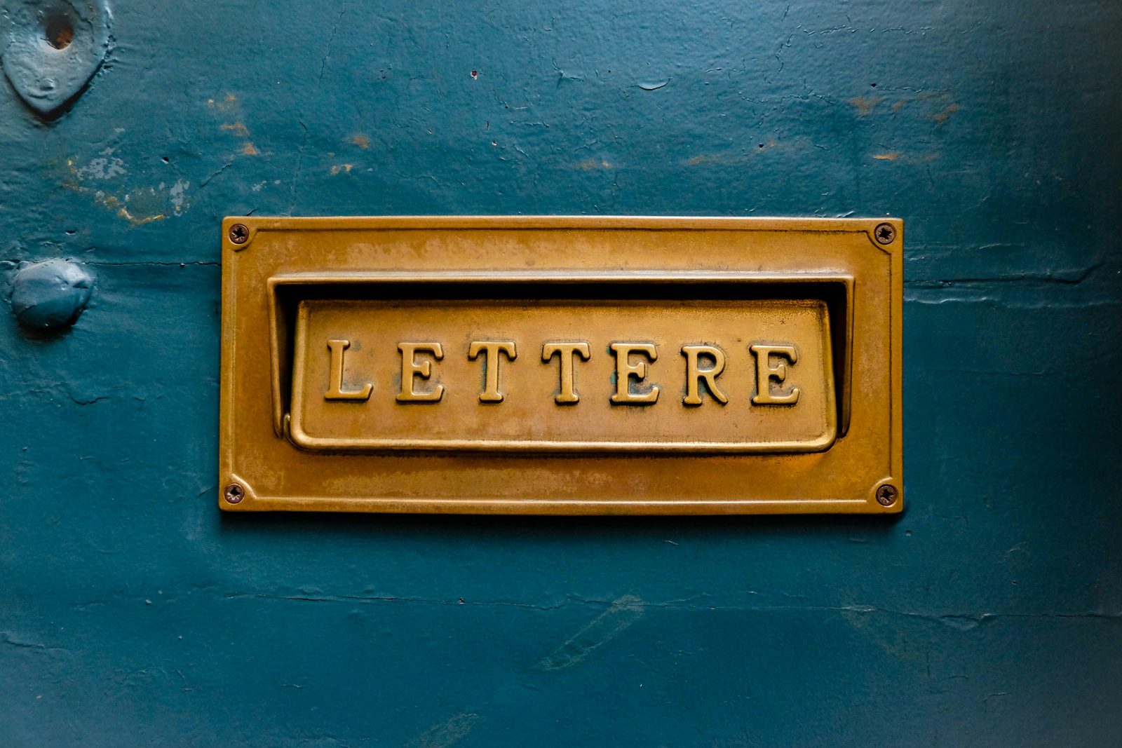 A brass mail slot labeled LETTERE on a weathered teal door.